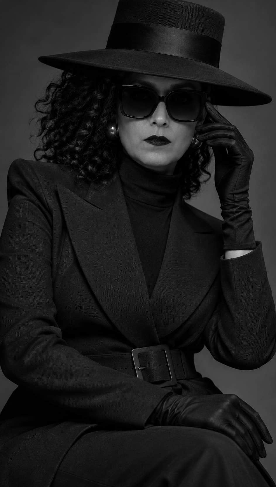 Florencia con sombrero de ala ancha, lentes oscuros y guantes negros, sentada con una mano en la sien.